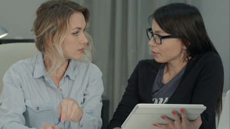 Two female colleagues brainstorming in the office using tabletの写真素材