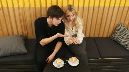 Happy couple using smartphone together and drinking coffee in cafeの写真素材