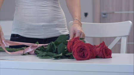 Young woman tying a ribbon bow on red rose bouquetの写真素材