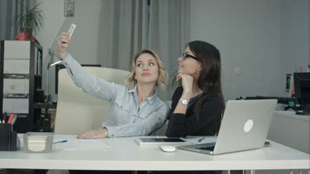 Two female colleagues taking selfie with phone in the officeの写真素材