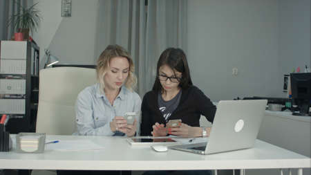 Senior manager showing young intern in glasses how to use mobile appの写真素材