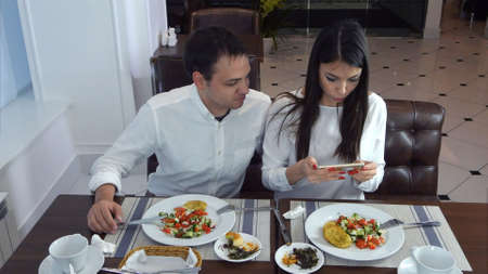 Young couple sitting in the restaurant and taking pictures of the food with mobile phoneの写真素材