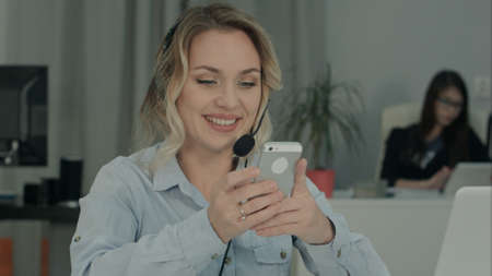 Smiling office woman texting on the phone at her workplaceの写真素材