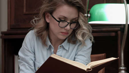 Serious young woman in glasses looking for informaton in the bookの写真素材