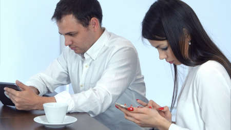 Two young people in cafe busy working with their phone and tabletの写真素材