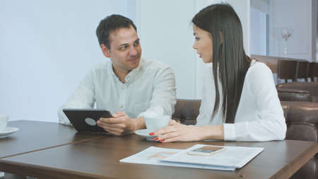 Excited woman telling story to her male coworker holding tablet during coffee breakの写真素材