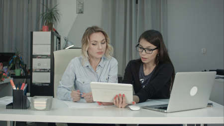 Two female professionals using digital tablet while working at the deskの写真素材