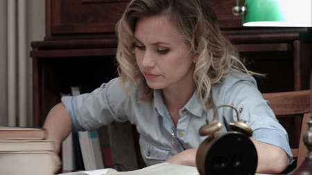 Pretty student fallen asleep on books at her desk and woken up by an alarmの写真素材