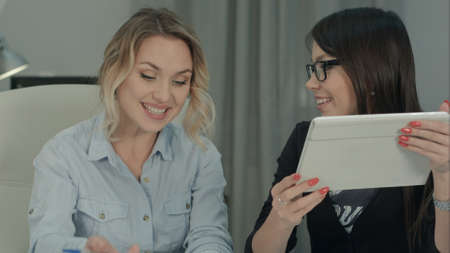 Businesswomen with digital tablet exchanging ideas in modern officeの写真素材
