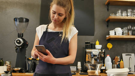 Delighted female barista using cell phone at work placeの写真素材