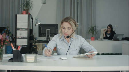 Efficient call operator making notes and using tablet while talking with customerの写真素材
