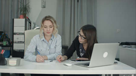 Blonde office woman drawing sketch while brunette coworker suggesting ideasの写真素材