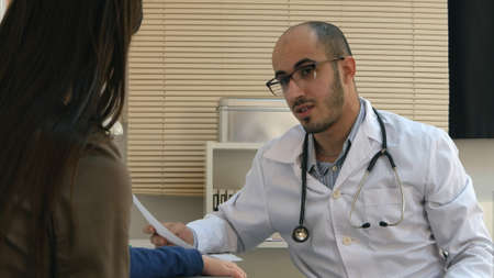 Young doctor in glasses explaining diagnosis to mother and her childの写真素材