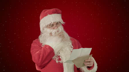 Santa Claus reading letters from children on red background with snowの写真素材