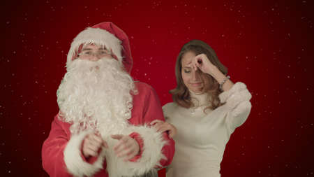 Beautiful christmas woman dancing with Santa Claus on red background with snowの写真素材