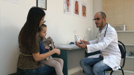 Pediatrician filling in medical form and giving pills to mother and her little daughterの写真素材