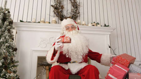 Good old Santa Claus sitting in a chair by the fireplace describing what presents he prepared for Christmasの写真素材