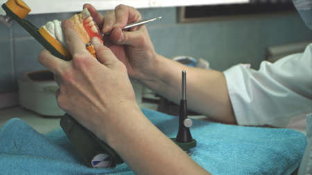 Dental technician removes excess wax from denture with a scalpel