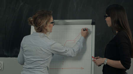 Two females standing and presenting graph on flipchart during business meetingの写真素材