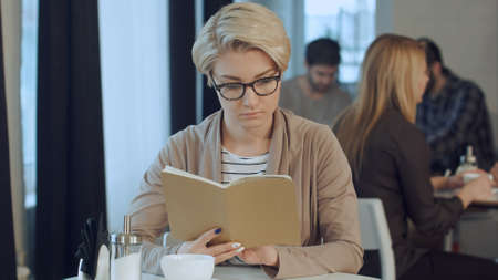 Sunday morning lifestyle scene of young hipster woman reading notes on her notebook in cafeの写真素材