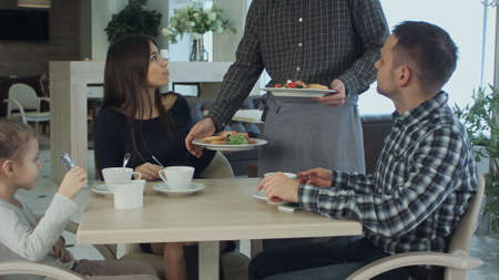 Young family take a meal in cafe or restaurant. Waiter make a mistake and confuse dishes. Father and mother looking angry and disappointed.の写真素材