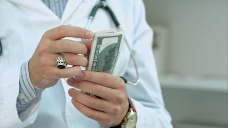 Male doctor counting money and putting it in his pocketの写真素材