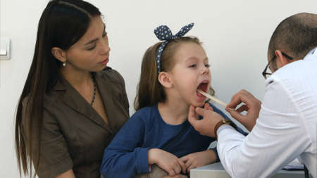 Male pediatrician examining throat of little girl sitting with her momの写真素材
