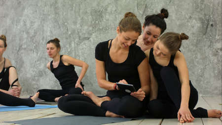 Portrait of smiling fit women using digital tablet while sitting at yoga mat after fitness workoutの写真素材
