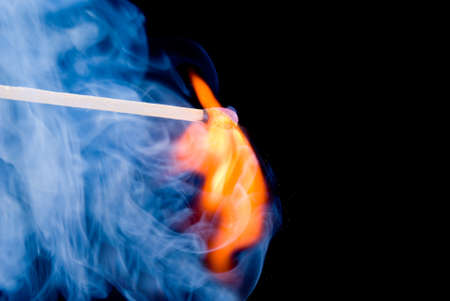 Burning match with blue smoke over black backgroundの写真素材