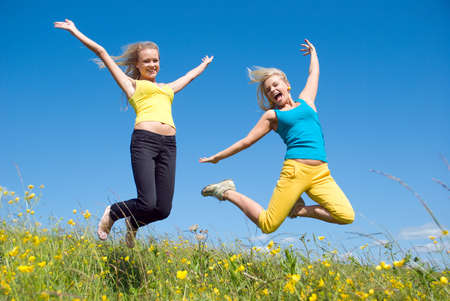 young woman jumping on background of the green meadow and blue skyの写真素材