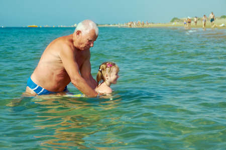 Swimming lesson grandfather and Little girl on the beachの写真素材