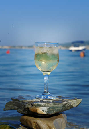 Glass of white wine by the coast.on the rocks, washed by the waves of the seaの写真素材