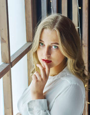 Pleased pretty woman with fair hair,green eyes and healthy skin dressed in white shirt,  posing holding her hand near mouthの写真素材