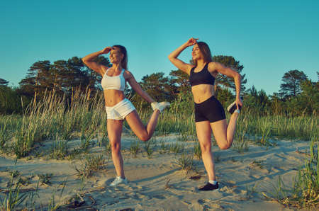 Two girls meditating practicing yoga fitness exercise at sunset  on the beach with a pine forest in the backgroundの写真素材