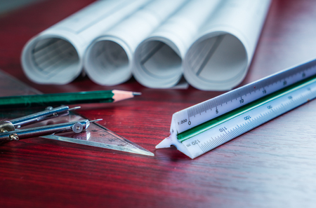 Architectural blueprints and blueprint rolls and a drawing instruments on the worktable