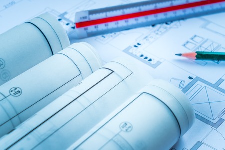 Architectural blueprints and blueprint rolls and a drawing instruments on the worktable