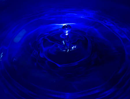 Deep blue water droplet hitting still surface of waterの写真素材