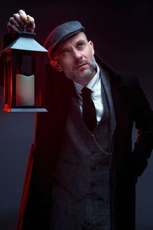 A man in a classic suit, coat and cap. stands. Holds a vintage lantern in his hand. Upward gaze. studio photography.の写真素材