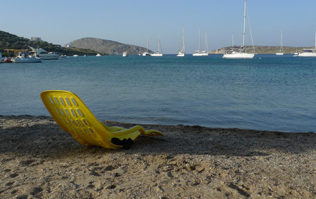A yellow plastic chair on the beach with yachts in the background, Leros island, Greeceの写真素材