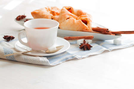 white china cup of black tea with teaspoon cubic sugar and fresh baked pastry