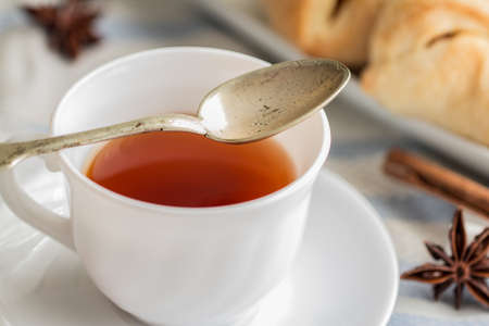 white china cup of black tea with teaspoon cubic sugar and fresh baked pastryの写真素材