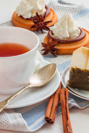 white china cup of black tea with teaspoon , teabag and  biscuit cakes with whipped cream topping on light blue kitchen towelの写真素材