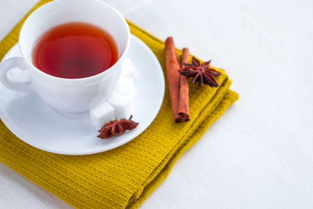 white china cup on  of black tea with silver teaspoon. anise and cinnamon sticks on green kithcen towelの写真素材