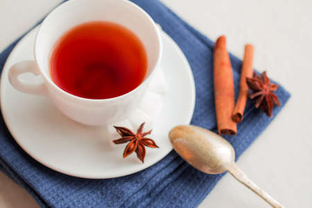 white china cup on  of black tea with silver teaspoon. anise and cinnamon sticks on green kithcen towelの写真素材