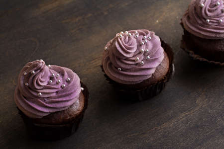 Chocolate cupcakes decorated with purple berries cream and silver sugar balls on brown wooden tableの写真素材