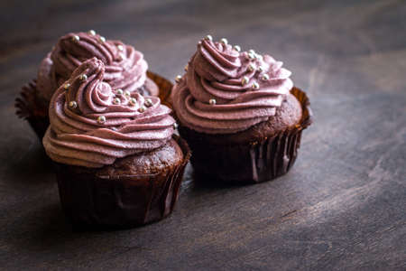 Chocolate cupcakes decorated with purple berries cream and silver sugar balls on brown wooden tableの写真素材