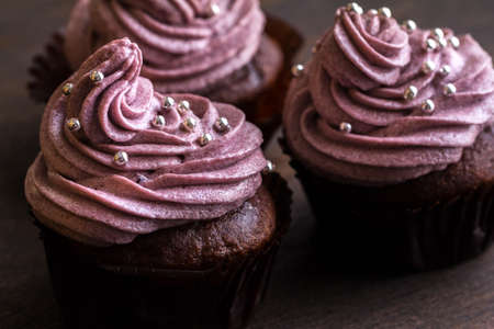 Chocolate cupcakes decorated with purple berries cream and silver sugar balls on brown wooden tableの写真素材