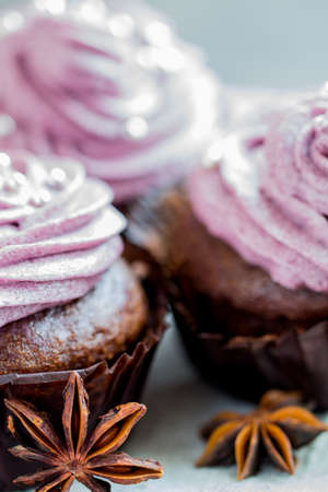 Chocolate cupcakes decorated with purple berries cream and silver sugar balls on brown wooden tableの写真素材