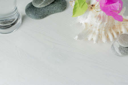 long glass of water on white wooden desktop with spa stones , seashell and bougainvillaeaの写真素材
