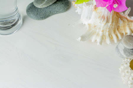long glass of water on white wooden desktop with spa stones , seashell and bougainvillaeaの写真素材